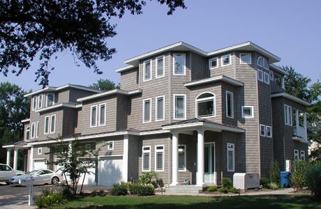 Modern three-story duplex house with gray siding and white windows, surrounded by trees under a clear sky.