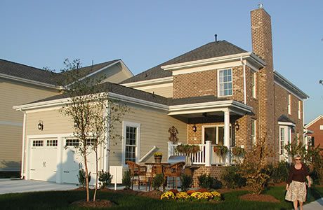 A woman walking by a newly built two-story suburban home with a brick facade, porch, and landscaped front yard.
