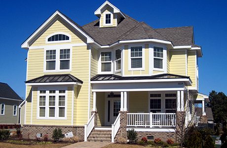 A yellow two-story house with white trim, a covered porch, and multiple gabled roofs under a clear blue sky.