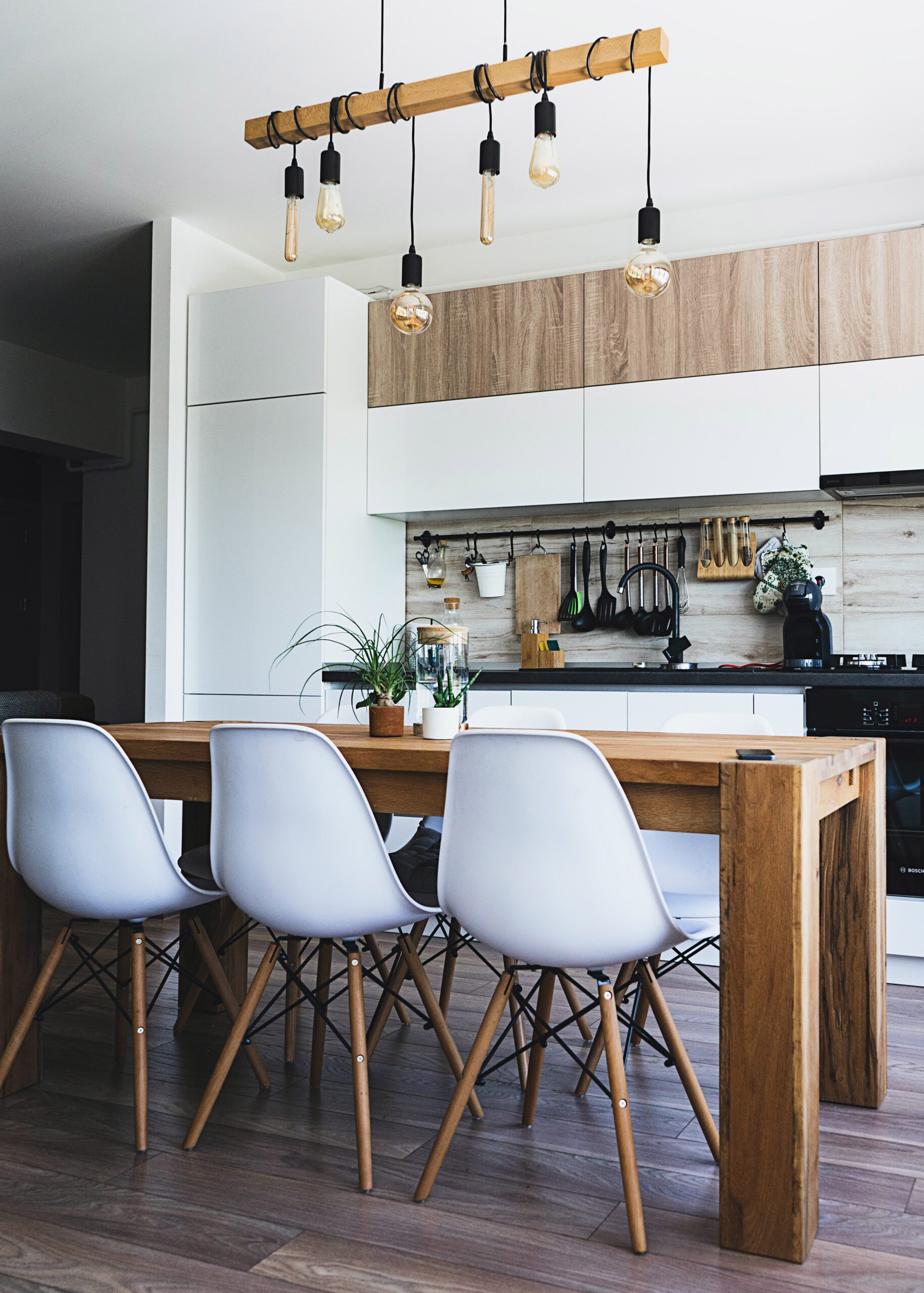 Modern kitchen interior with a wooden island, white chairs, pendant lights, and black accents.