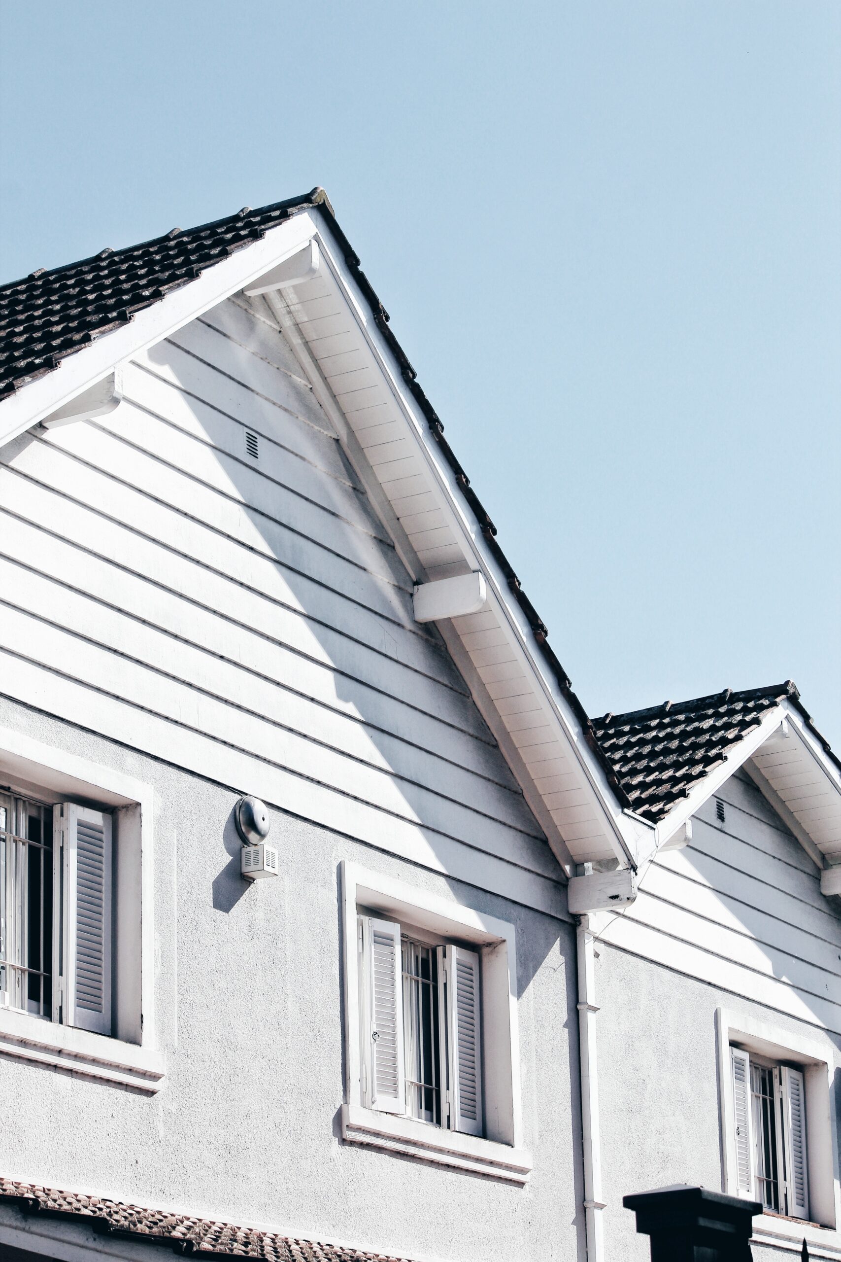 White house with a gabled roof, visible shutters, and a clear blue sky in the background.
