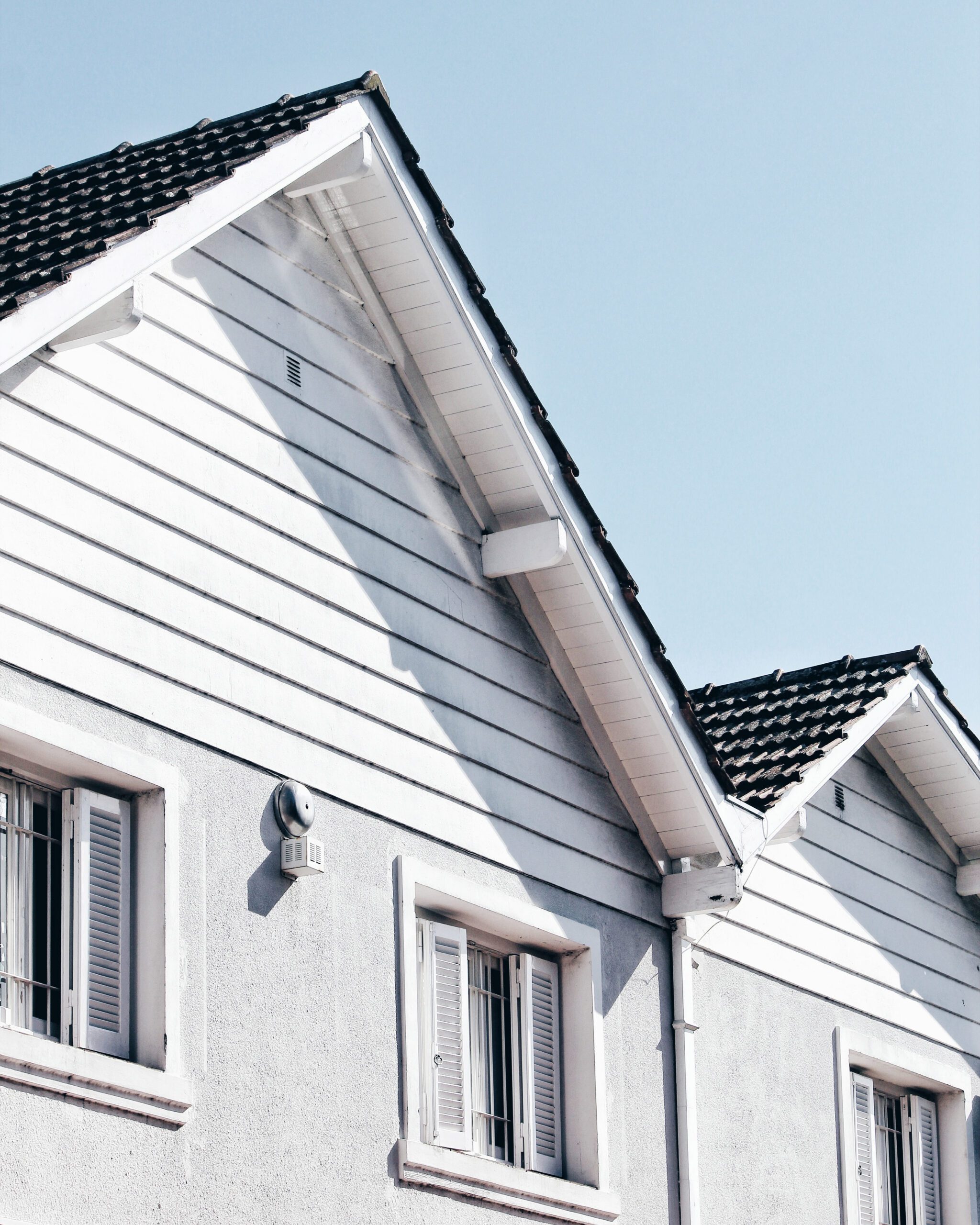 White suburban house with a black shingle roof under clear blue skies.