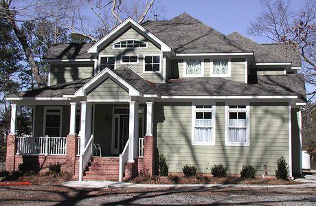 Two-story green house with a gabled roof, white trim, front porch, and a clear blue sky in the background.